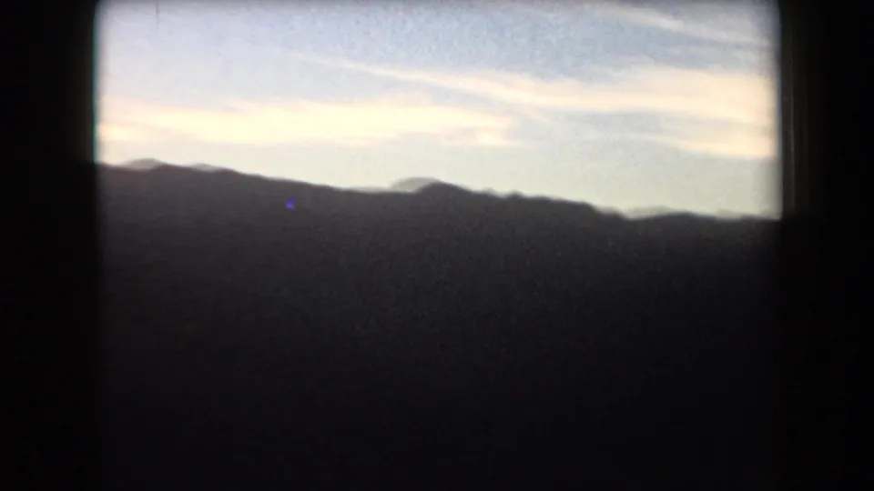 1958 Arizona home-movie view of dark low ridges and distant mountain shapes beneath a bright sky with soft clouds.