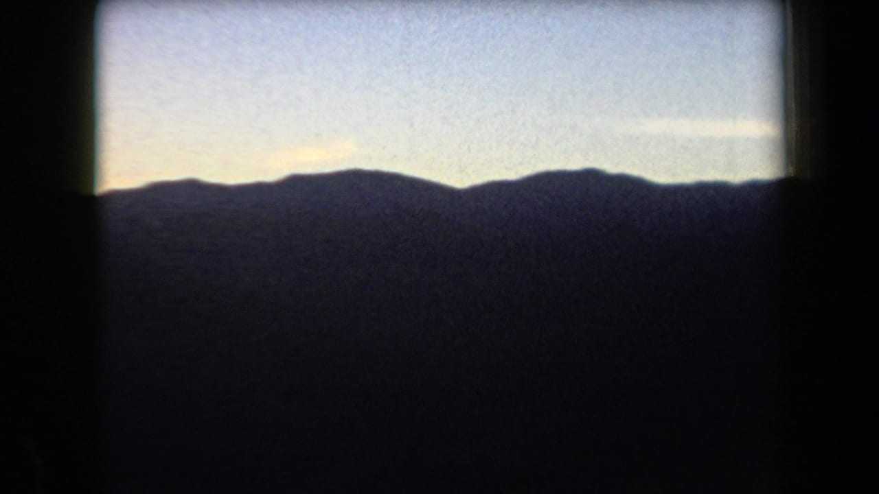 1958 Arizona 8mm frame showing a dark mountain horizon beneath a fading blue sky with warm light near the ridge.