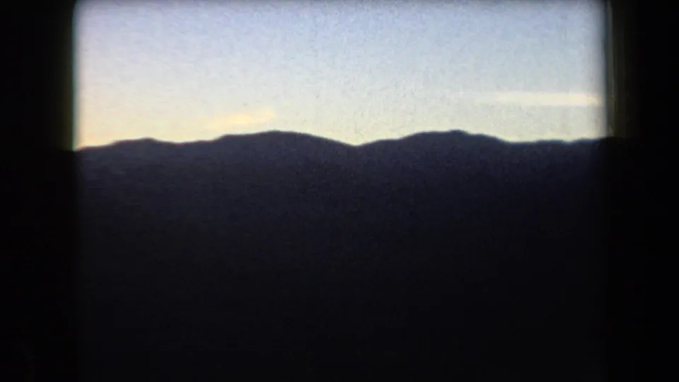 1958 Arizona 8mm frame showing a dark mountain horizon beneath a fading blue sky with warm light near the ridge.