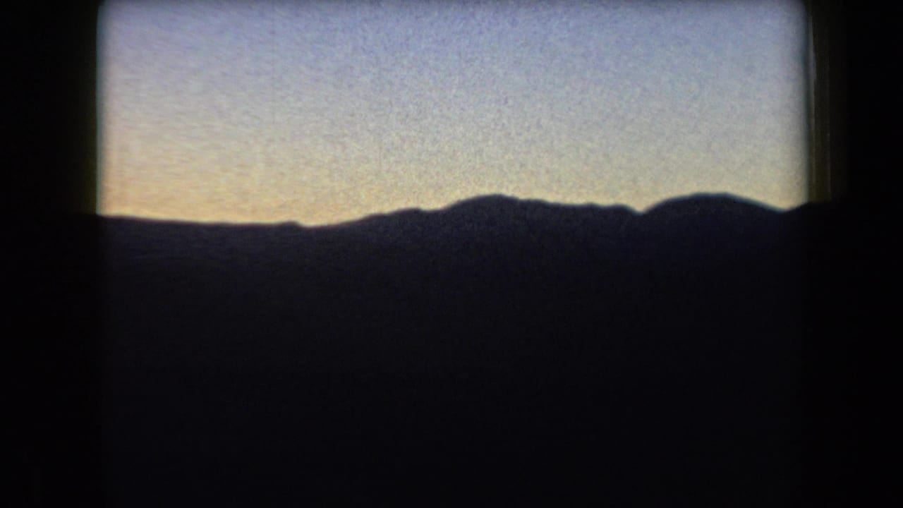 Low dark ridge line under a pale evening sky with visible film grain.
