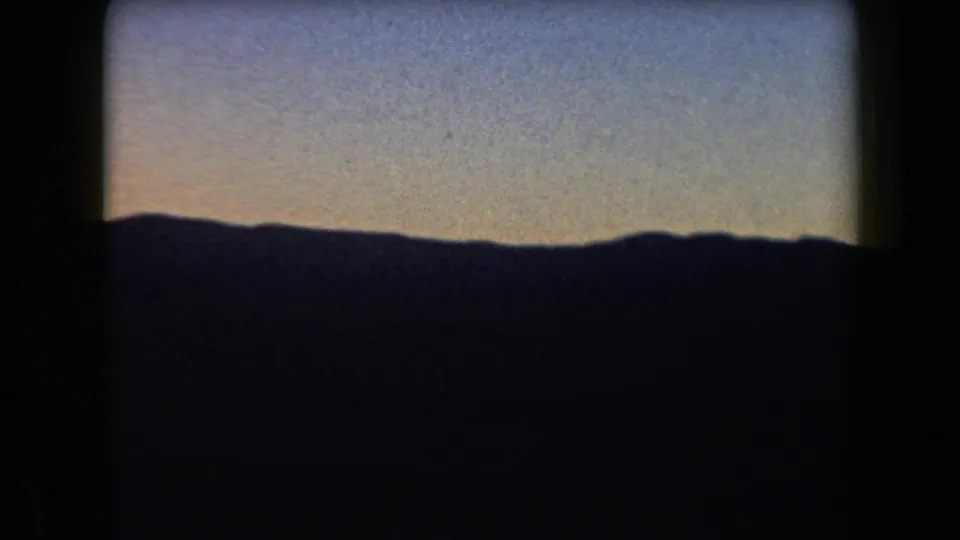 1958 Arizona 8mm frame showing distant hills in silhouette, with a broad grainy blue sky and faint warm color near the horizon.