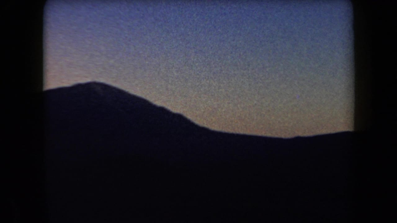 1958 Arizona home-movie frame showing a dark mountain silhouette against a fading twilight sky.