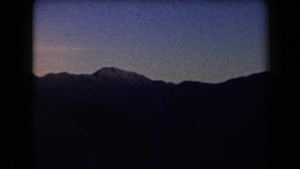 Jagged mountain range in deep shadow below a blue evening sky.
