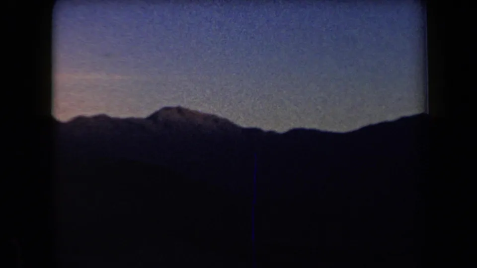 Arizona mountain ridgeline appears in silhouette under a dim blue twilight sky in 1958 8mm footage.