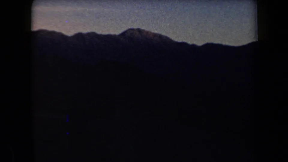 A dark Arizona mountain range fills the lower frame beneath a muted twilight sky in archival 8mm footage.