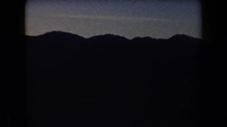 Final 1958 Arizona frame with a broad mountain silhouette and grainy blue-purple evening sky.