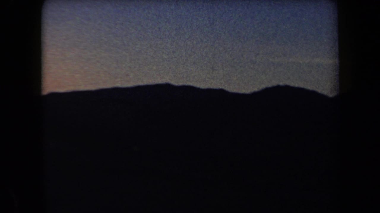1958 Arizona 8mm frame showing a dark mountain silhouette under a dim, grainy twilight sky.