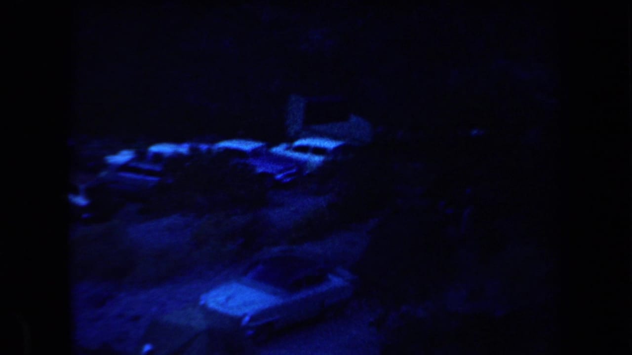 1958 Arizona home-movie frame showing parked cars and caravans at a dark blue-lit night campsite.