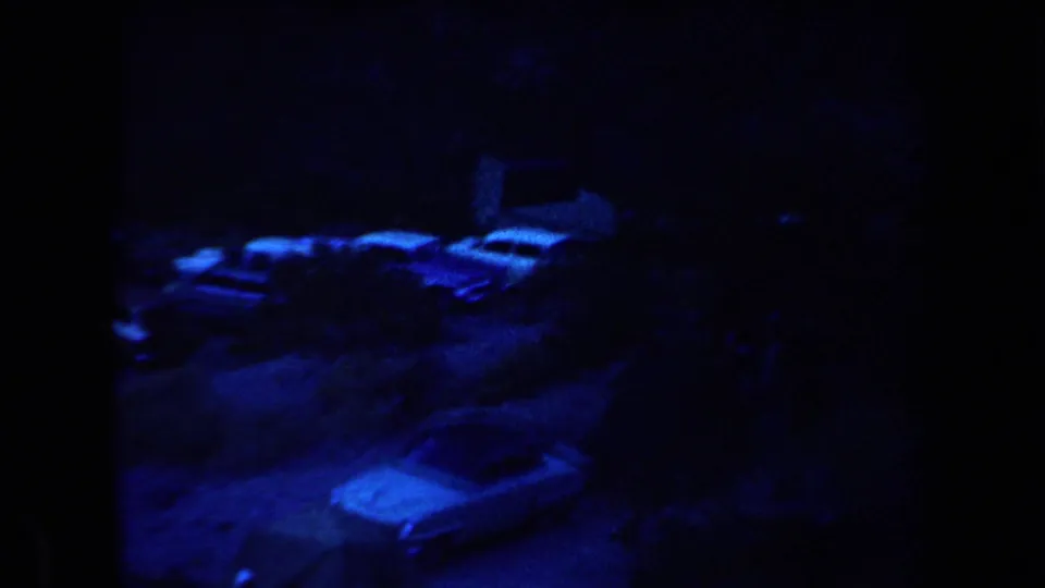 1958 Arizona home-movie frame showing parked cars and caravans at a dark blue-lit night campsite.