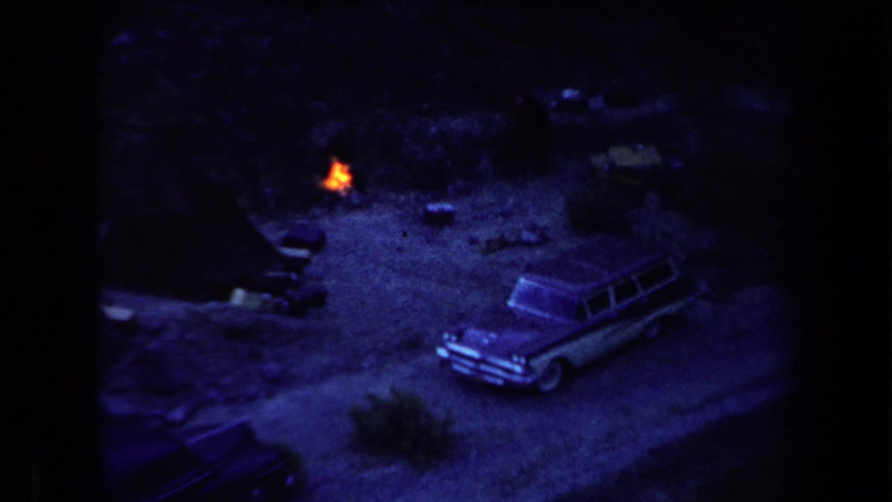 1958 Arizona home-movie frame showing a small orange campfire near a parked station wagon in a dark dirt clearing.