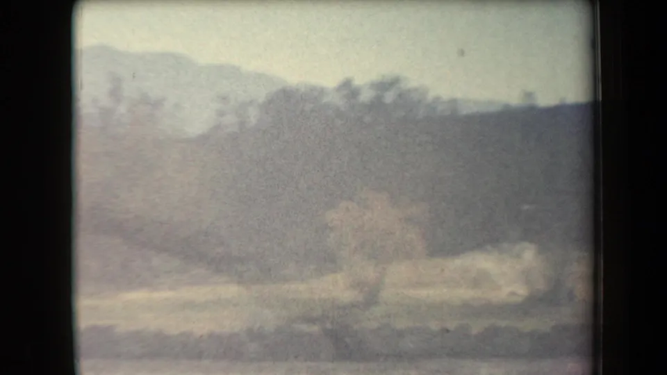 Washed-out 8mm frame from the same 1958 Arizona camping clip, with the station wagon faintly visible against pale hills or brush.