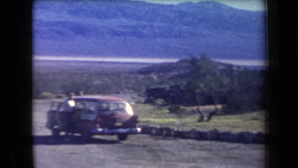 Red mid-century station wagon near a low roadside wall in 1958 Arizona desert scenery with distant mountains.