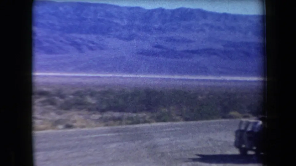 Curving Arizona road with desert brush and mountain backdrop, with part of the station wagon visible at the right edge.