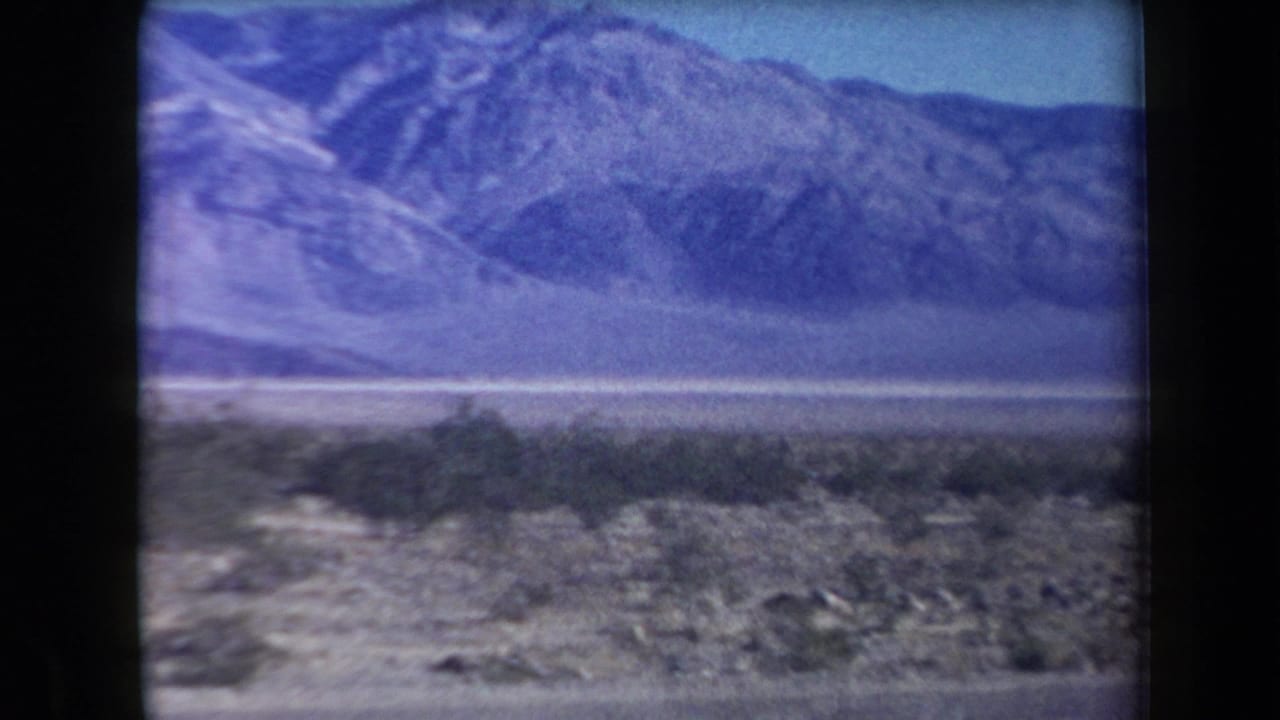 Rugged mountain range beyond flat desert scrub and a roadside foreground.