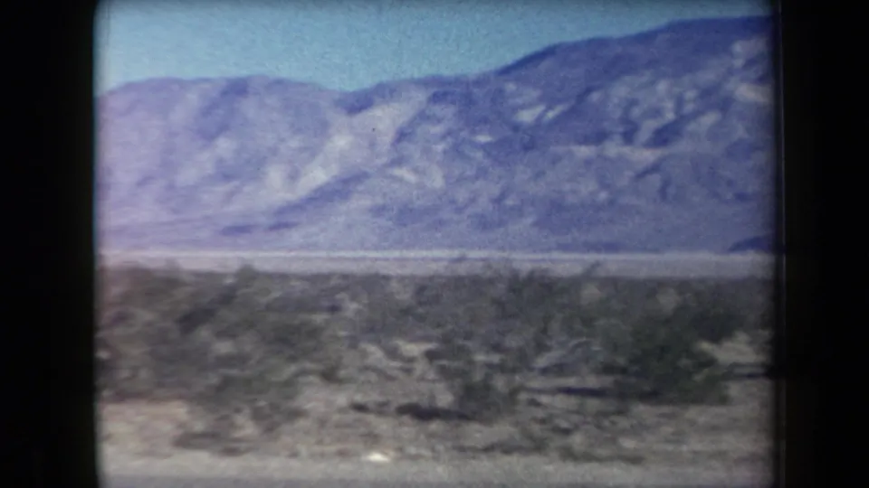 1958 Arizona travel footage frame showing scrubby desert foreground and a hazy mountain range beyond.