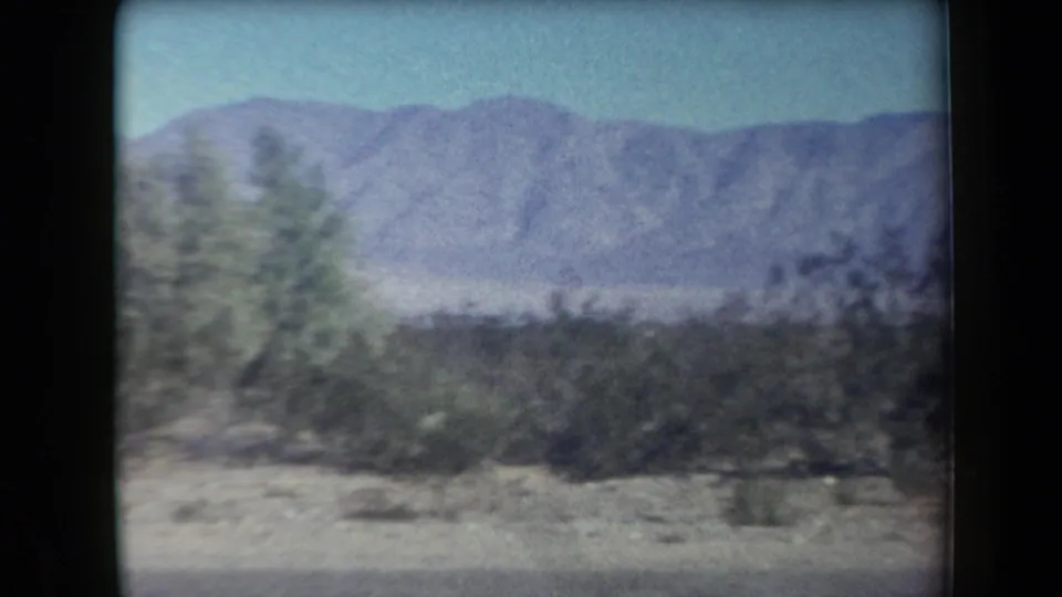 1958 Arizona desert view with moving-vehicle blur across shrubs, low roadside ground, and a distant mountain ridge.