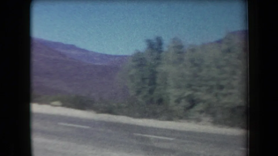 1958 Arizona roadside view with a paved road curving past desert vegetation and purple-toned mountains in the background.