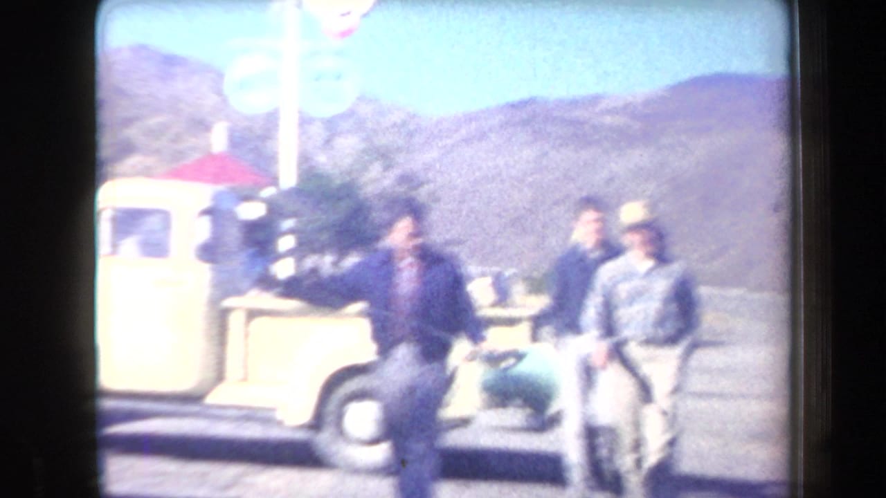 Men stand near a yellow pickup truck with mountains and a swim-pool sign behind them.