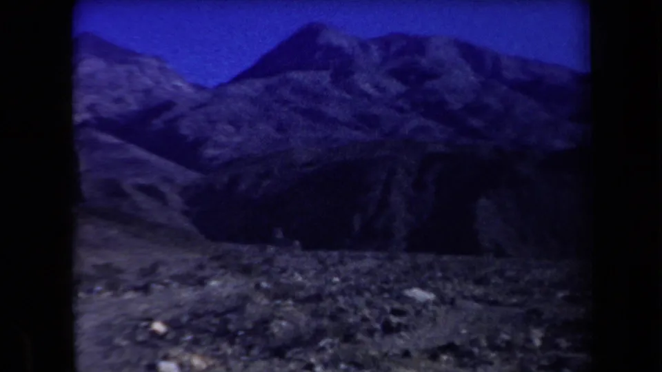 1958 Arizona home-movie frame of shadowed desert mountains, rough foreground ground, and strong blue color shift.