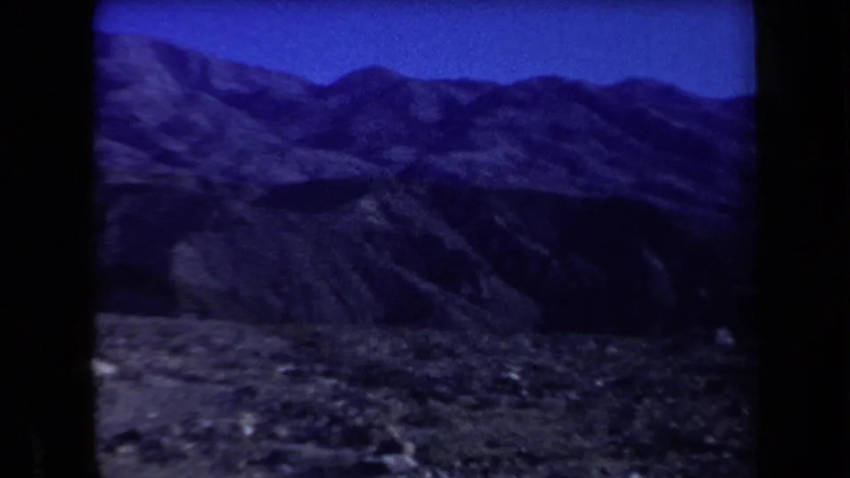 1958 Arizona home-movie frame showing layered mountain ridges and arid foreground terrain in blue-shifted 8mm color.