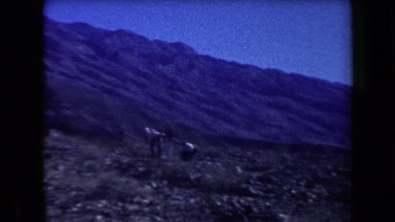 Small group of people walking across rocky ground beneath a mountain ridge.