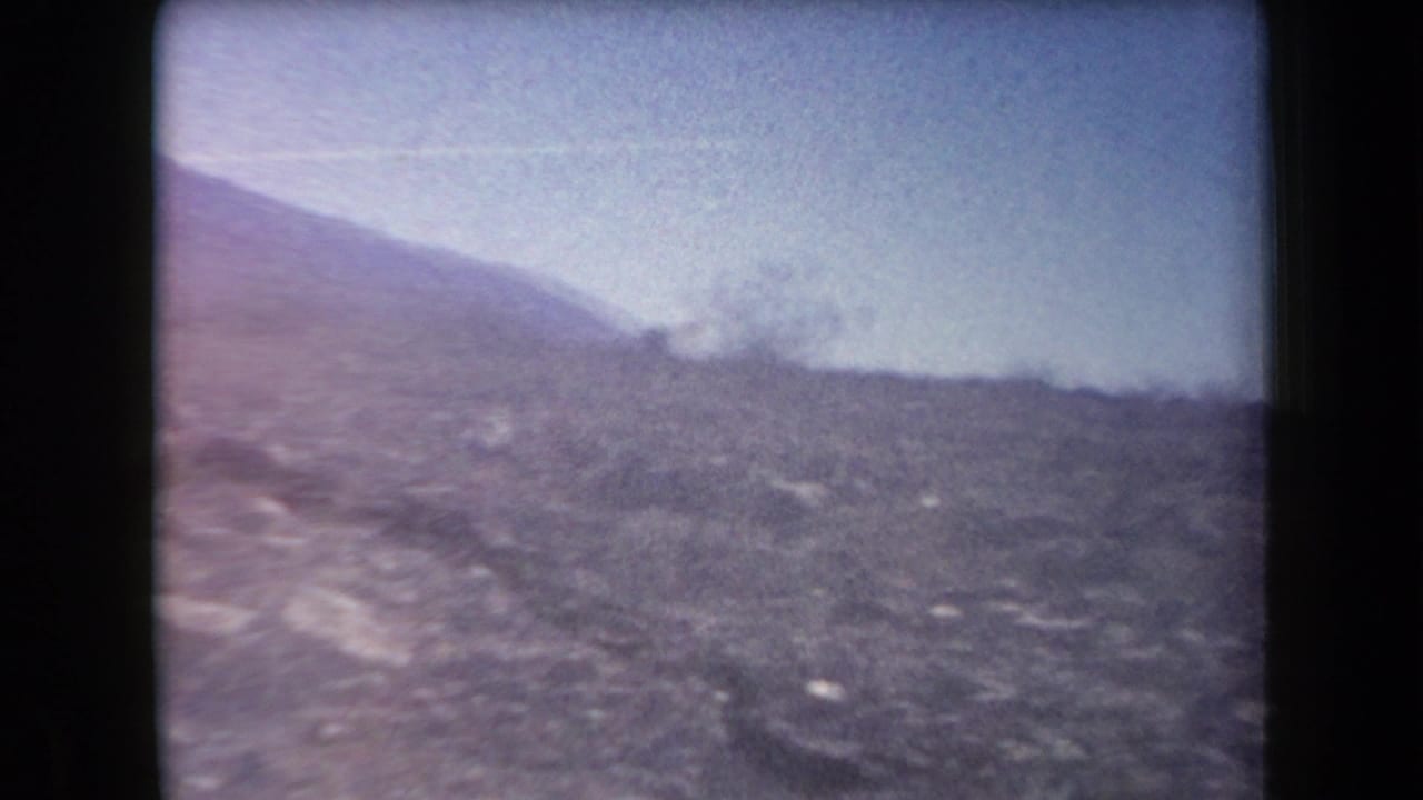1958 Arizona 8mm frame showing rocky desert ground, low hills, and distant mountains in soft, faded color.