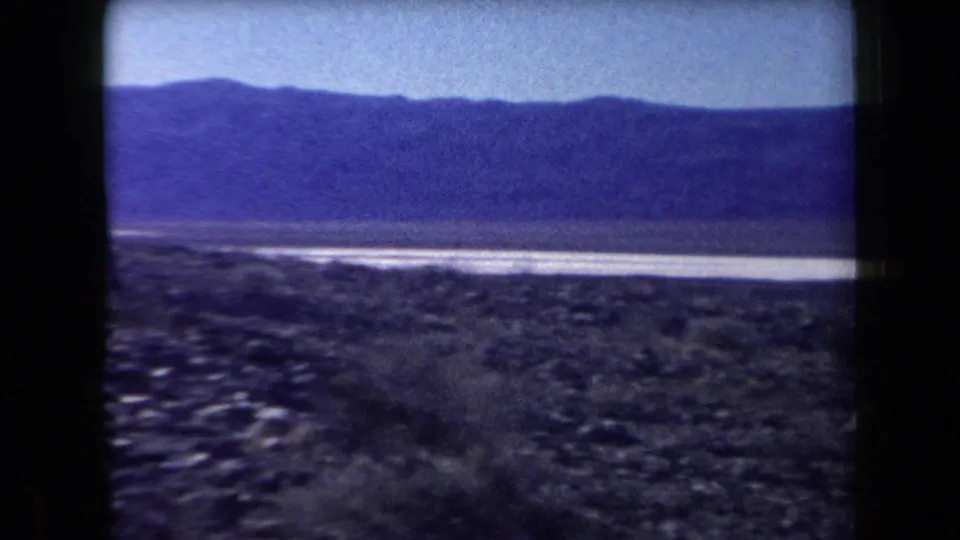 1958 Arizona 8mm landscape with rocky foreground, a pale water or salt-flat band, and mountains in the distance.