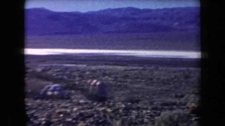 Arizona desert landscape with scattered rocks, low scrub, a bright flat stretch, and mountains across the horizon.