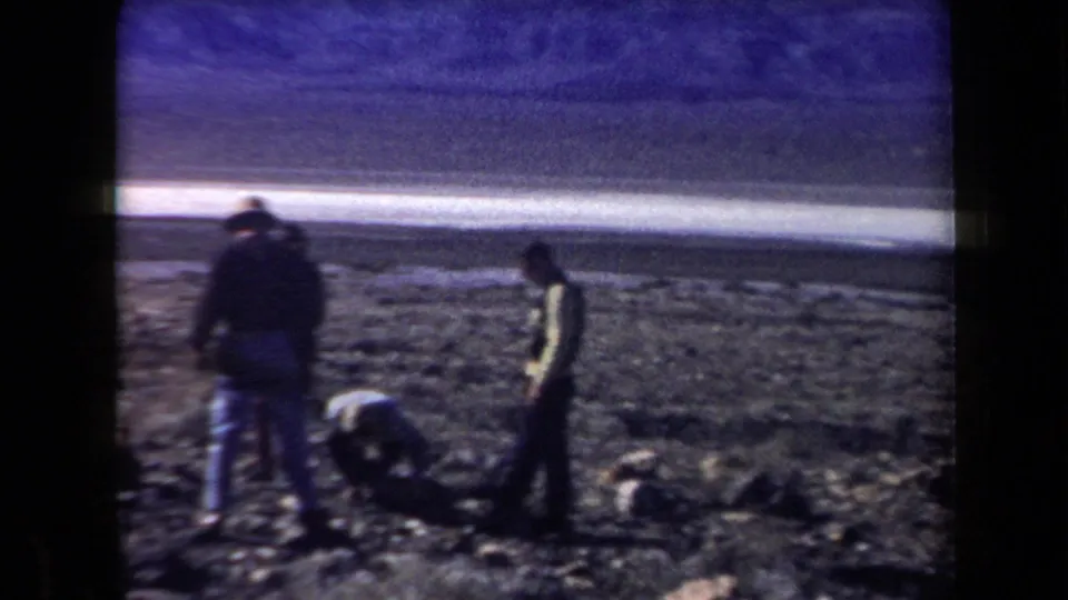 People in 1958 Arizona appear to examine or collect material from rocky desert ground near a salt-flat edge.