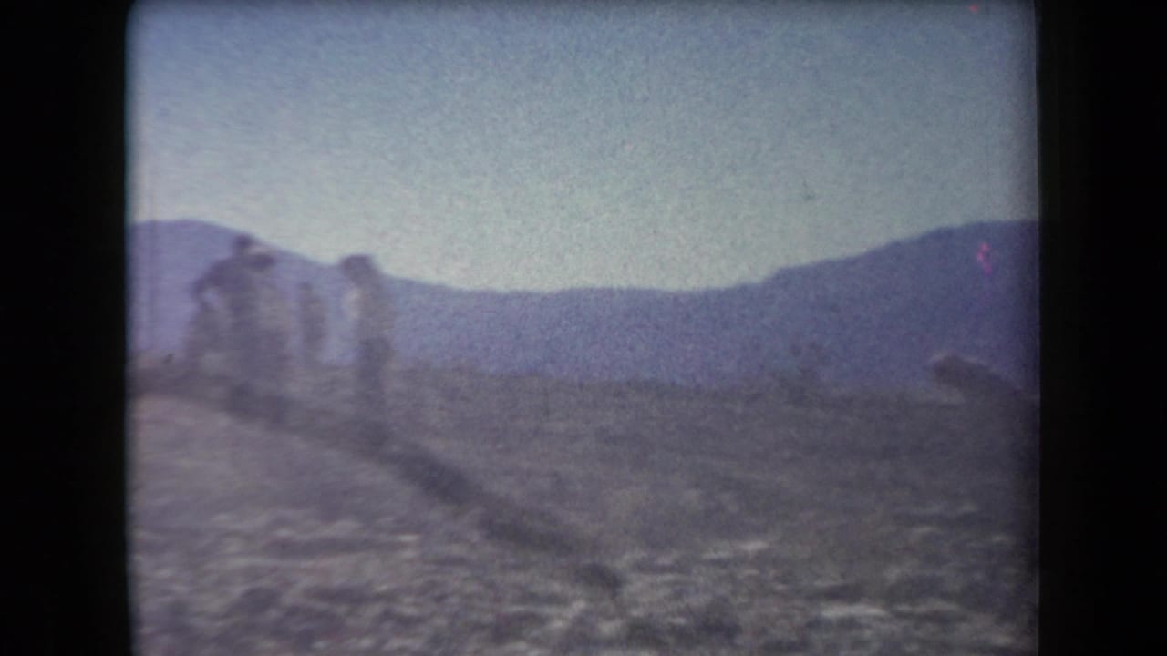 In 1958 Arizona home-movie footage, several distant people appear on rocky desert terrain with low mountains behind them.
