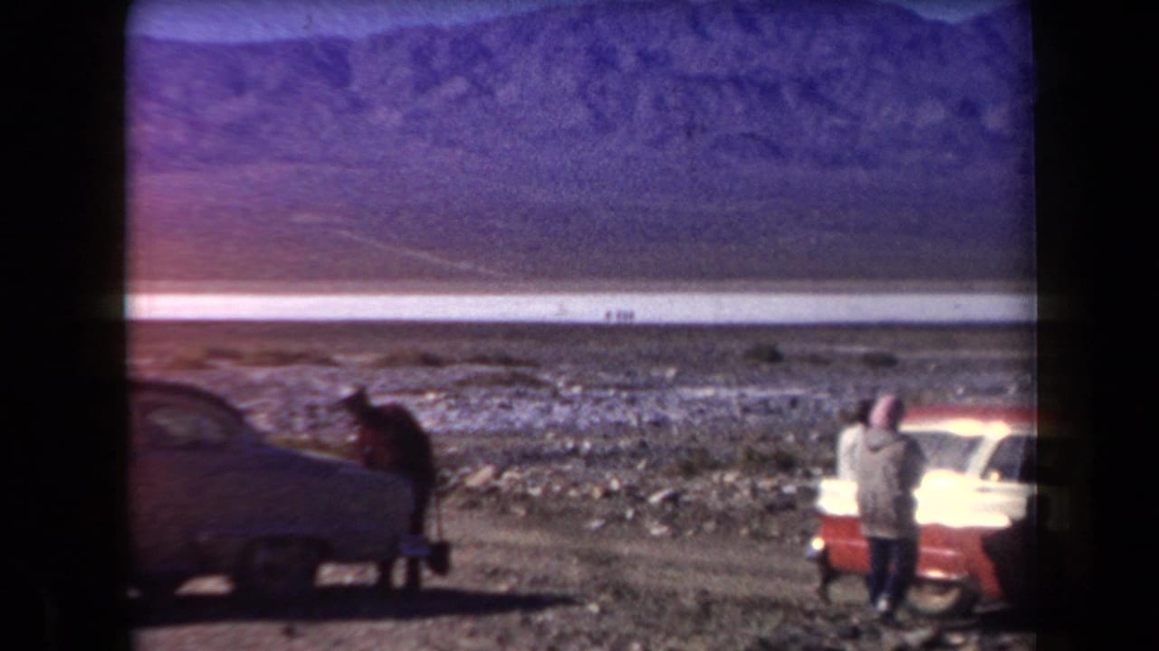 In the supplied 1958 Arizona home-movie clip, adults pause beside classic cars near a broad desert plain and distant mountains.