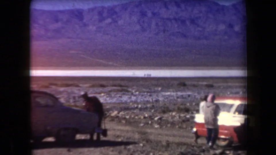 In the supplied 1958 Arizona home-movie clip, adults pause beside classic cars near a broad desert plain and distant mountains.