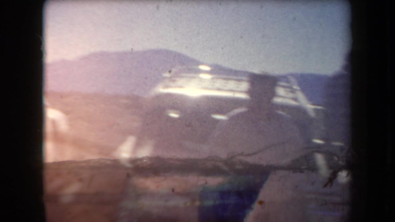 1958 Arizona 8mm frame showing hazy desert terrain, distant hills, strong exposure flare, and physical film borders.