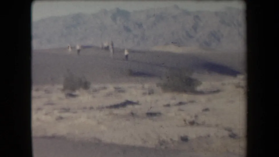 1958 Arizona home-movie frame with tourists as small figures across a desert flat below distant hills.