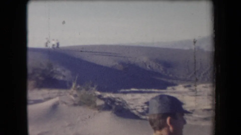 1958 Arizona home-movie frame showing a capped observer near desert dunes, scrub, and distant mountains.