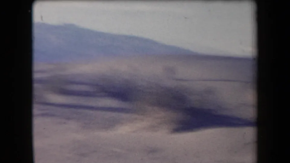 Soft 8mm view of an Arizona desert slope with distant mountains and a washed pale sky.