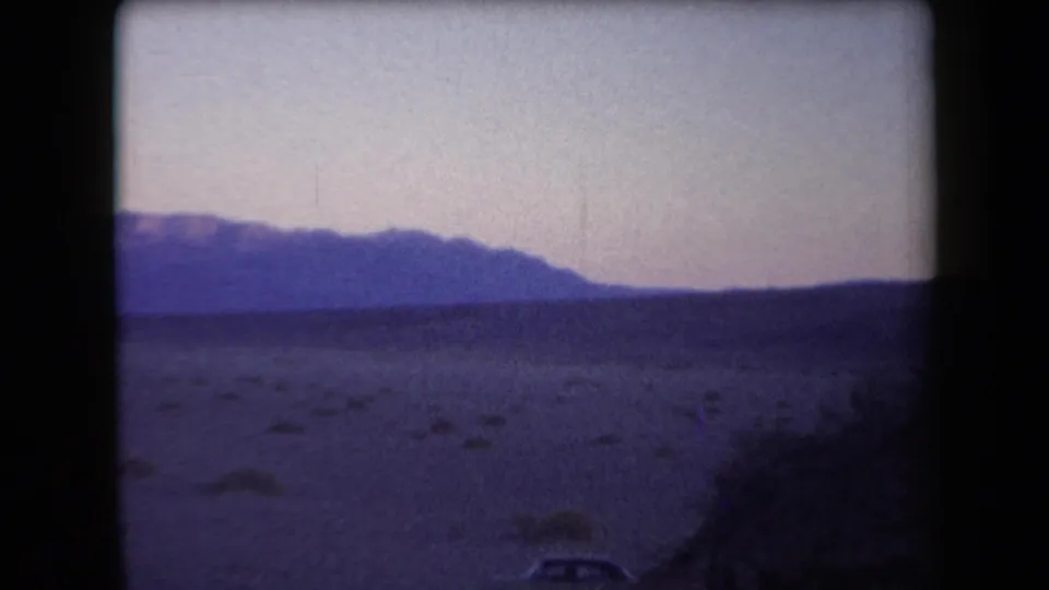 Wide 1958 Arizona desert view with sparse scrub, a dark mountain horizon, and faded 8mm color.