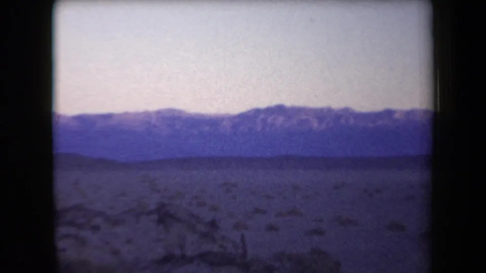 Arizona 1958 8mm view across sparse desert brush toward a purple-blue mountain range at dusk.