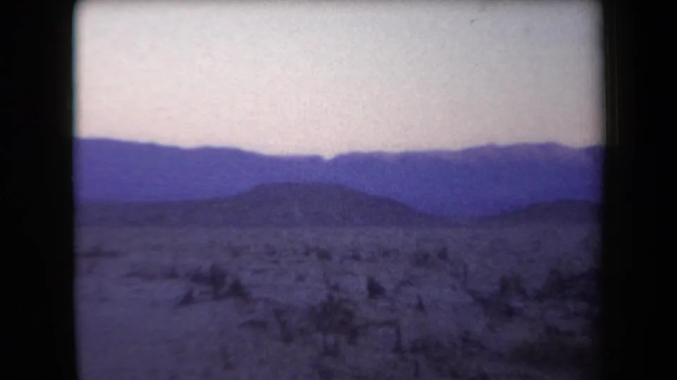 Arizona 1958 8mm frame showing scrubby desert foreground and layered blue mountain silhouettes in dusk light.