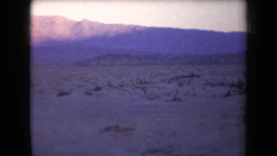 Arizona desert landscape from 1958 with sandy ground, scattered brush, and layered mountains under faded color.