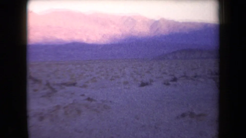 1958 Arizona home-movie frame with magenta-pink mountain light, dry terrain, and low desert vegetation.