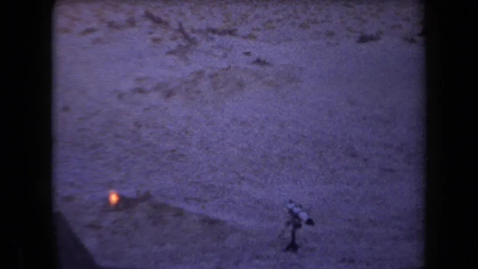 1958 Arizona desert frame showing scrubby terrain, a small orange ground light, and an indistinct dark upright shape.