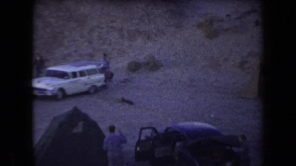 1958 Arizona 8mm frame showing a white station wagon, tent camp, and people on sandy desert terrain.