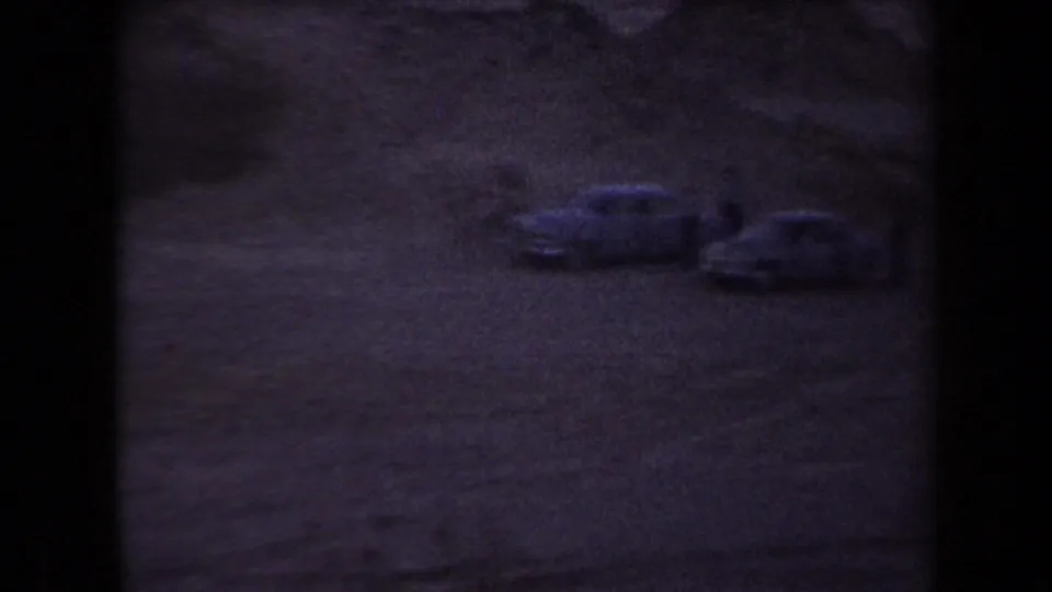 Dark 1958 Arizona 8mm frame with two classic cars parked across a dusty field.