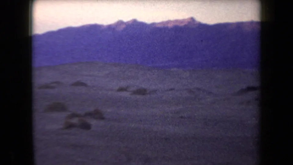 Wide 1958 Arizona desert view with sandy foreground, scattered low shapes, and distant mountains.
