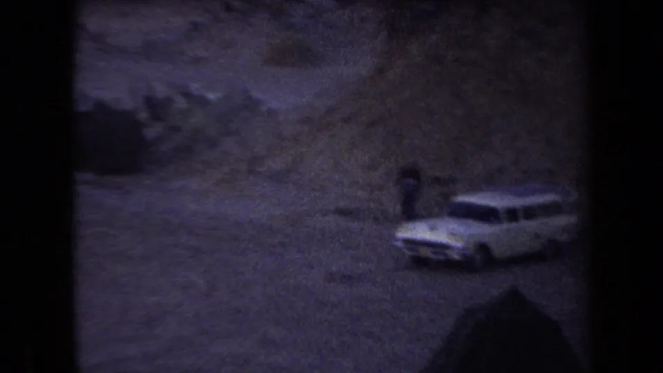 1958 Arizona 8mm frame with a white station wagon near a desert campsite, tents, and a small figure in the fading light.