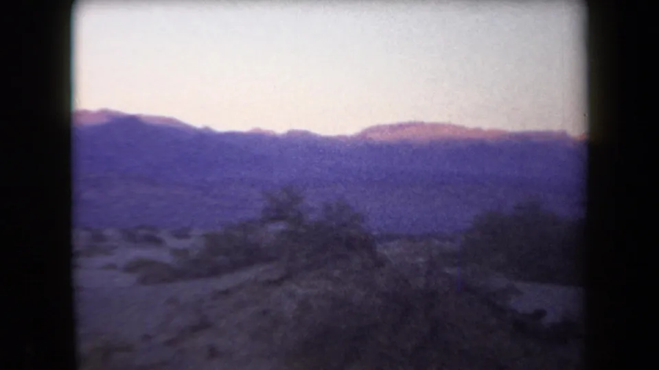 1958 Arizona home-movie frame with purple-blue mountain silhouettes, pale sky, desert scrub, and visible film gate borders.