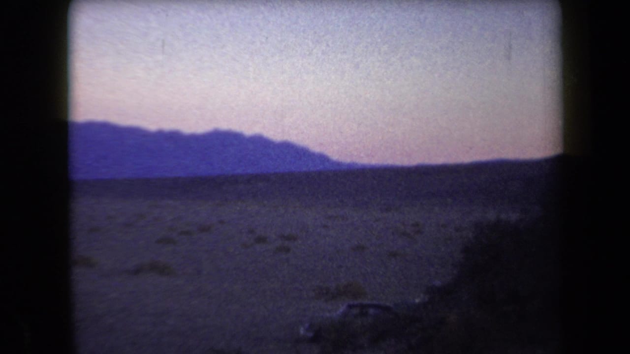 1958 Arizona 8mm frame showing dark desert foreground, distant mountain silhouettes, and a muted purple-pink evening sky.