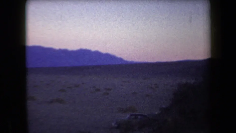 1958 Arizona 8mm frame showing dark desert foreground, distant mountain silhouettes, and a muted purple-pink evening sky.