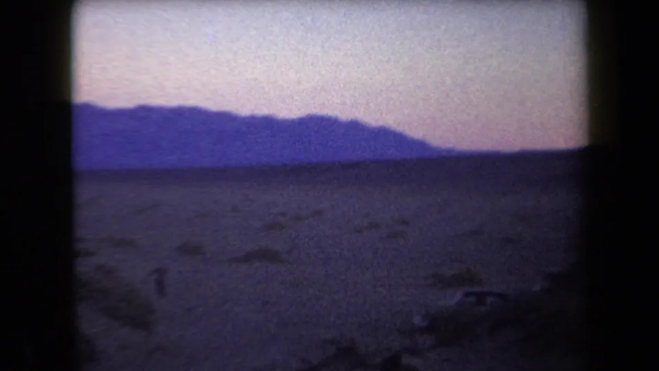 1958 Arizona home-movie frame of an arid plain and dark mountain ridge beneath a softly colored twilight sky.